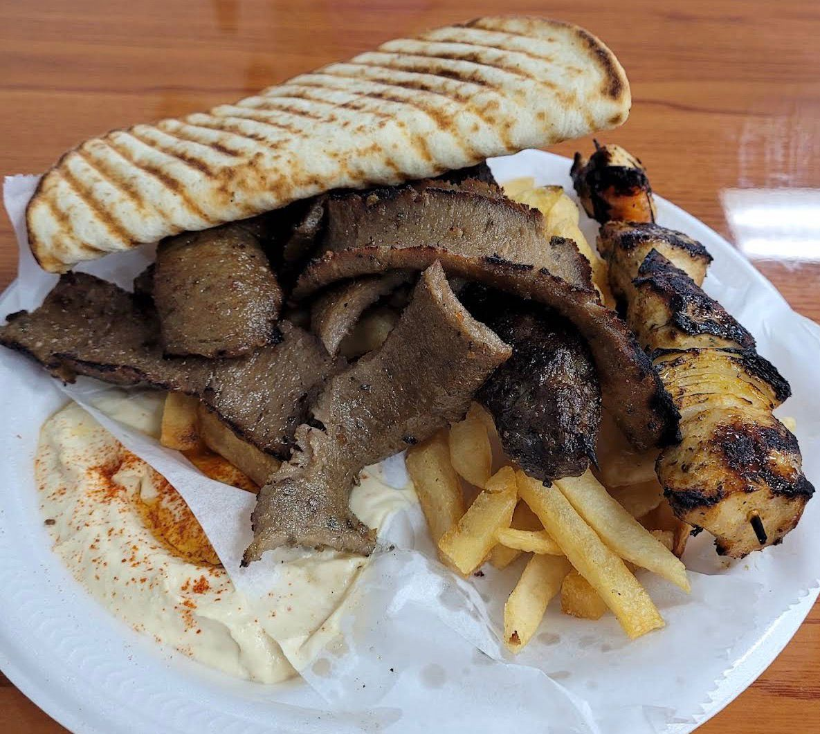 Mixed grill plate with gyro meat, chicken skewer, fries, hummus, and grilled pita from Samad Grill